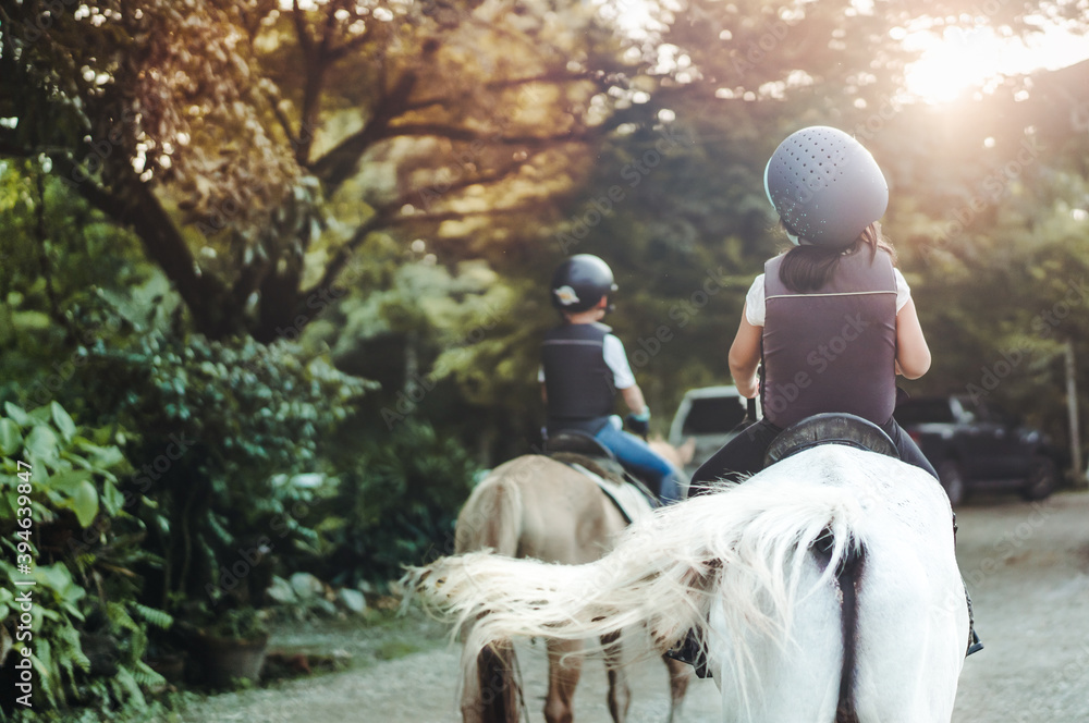 骑马者。后视孩子们学习骑马。快乐的亚洲小女孩在马校骑马f