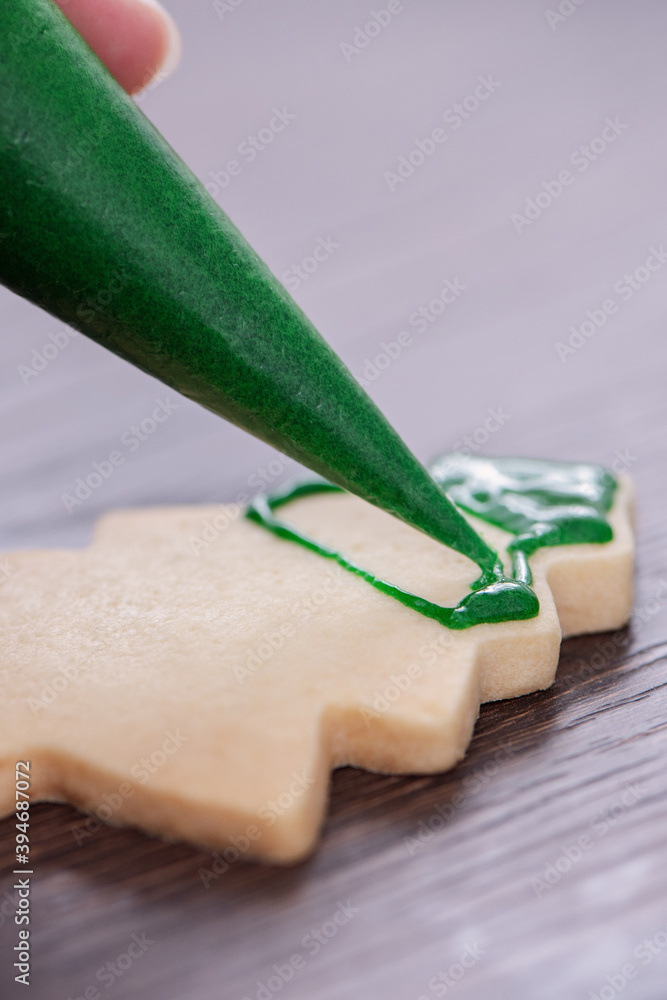 用糖霜在木桌背景上画圣诞树糖饼干的特写。