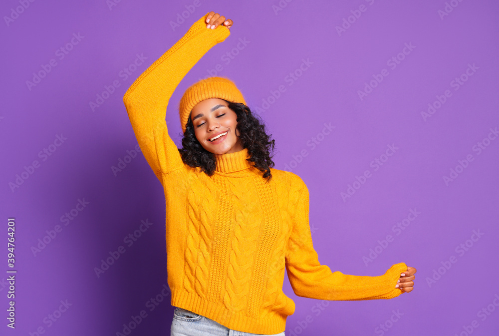 穿着黄色毛衣、戴着帽子的开朗的非裔美国妇女跳舞，享受多姿多彩的生活