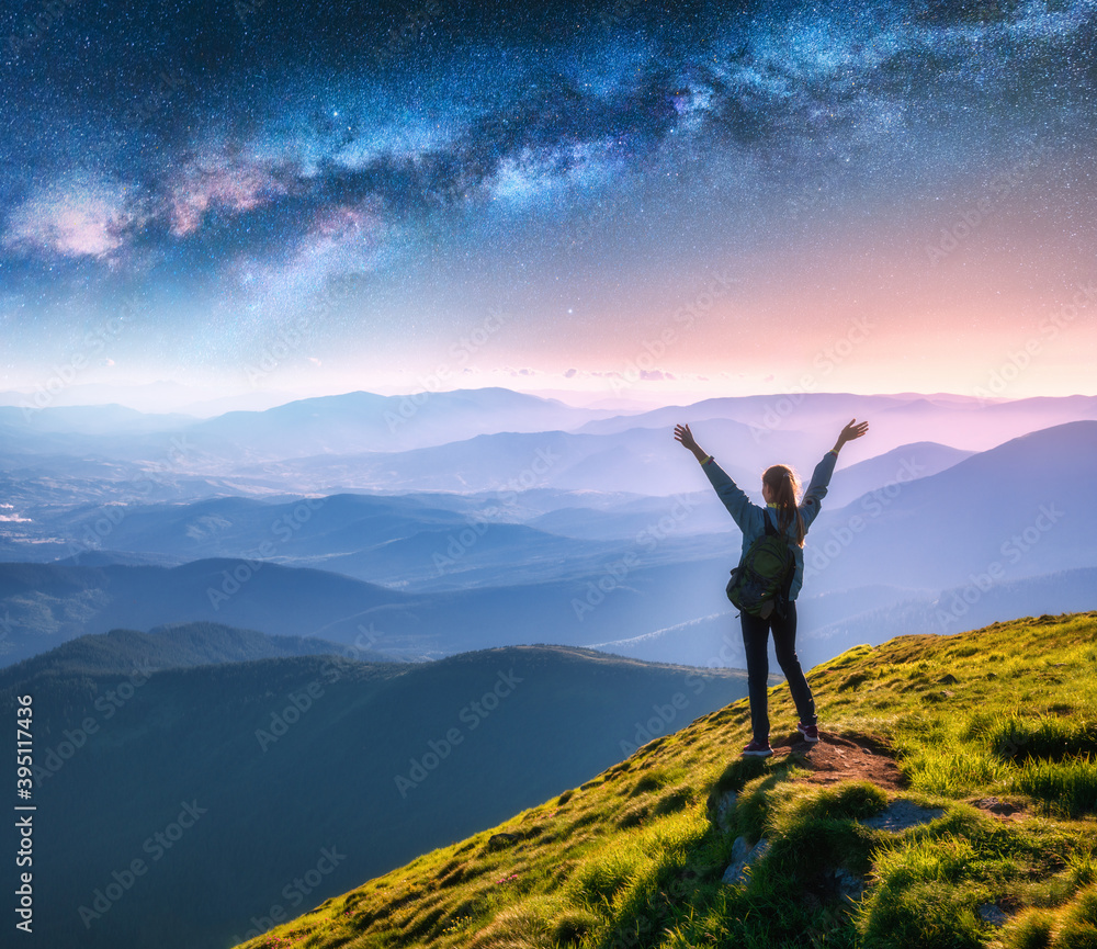 Happy young woman on the mountain peak and arched Milky Way over mountains at night. Landscape with 