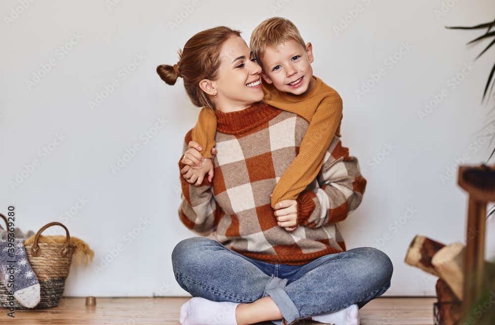 happy family mother and loving son in warm sweaters hug and laugh sitting on floor near wall  at hom