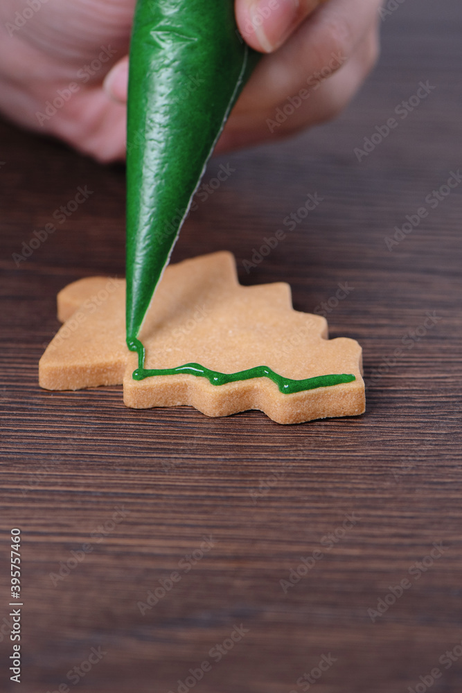 用糖霜在木桌背景上画圣诞树糖饼干的特写。