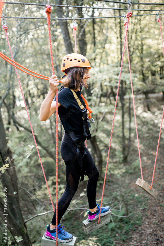 一位装备精良的年轻女士正在积极娱乐，在公园里爬绳索，排除障碍