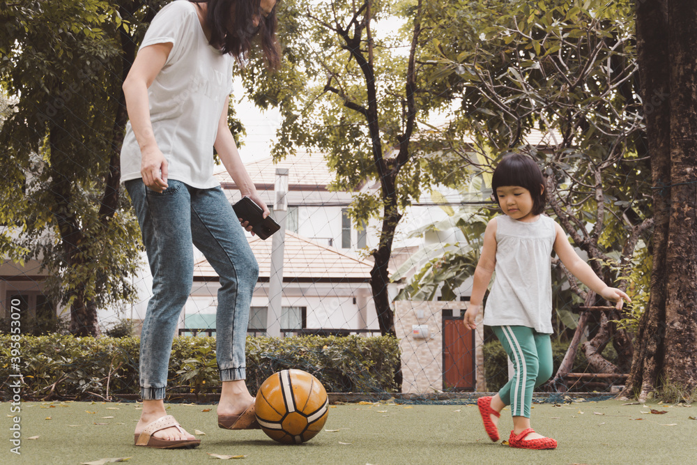 亚洲3岁的孩子和妈妈在公园里踢足球。有趣的生活和家庭游戏时间的背景。