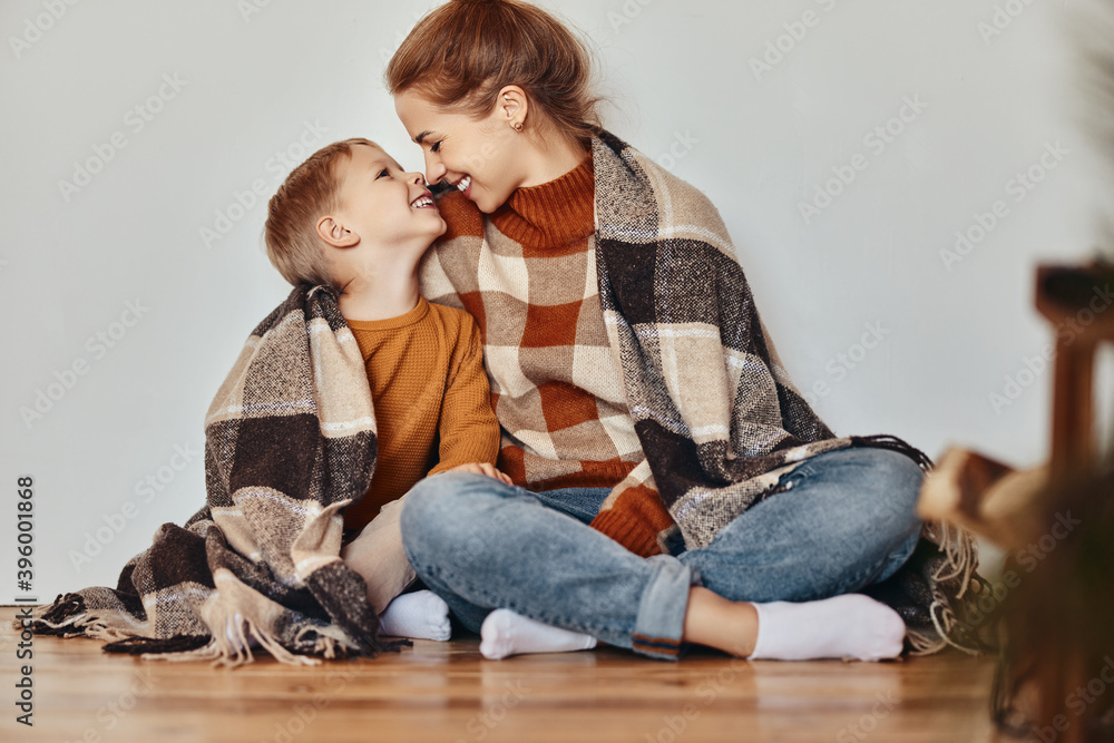 幸福的家庭母亲和慈爱的儿子晚上在家里裹着温暖的毯子拥抱大笑。