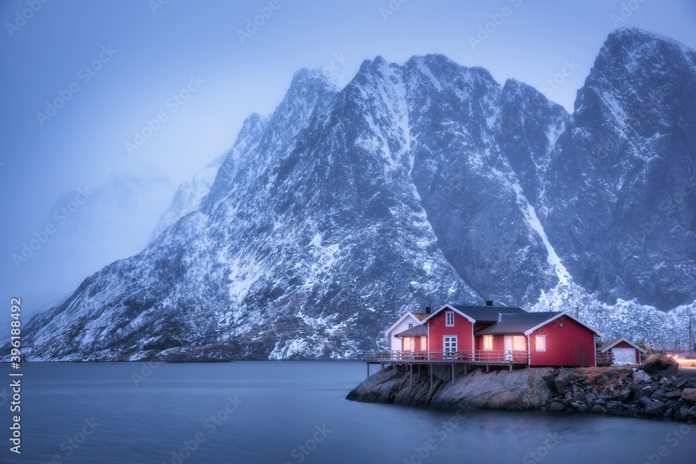 黄昏时，海岸上的红色罗布和雾中被雪覆盖的山脉。挪威罗弗敦群岛。穆迪冬季