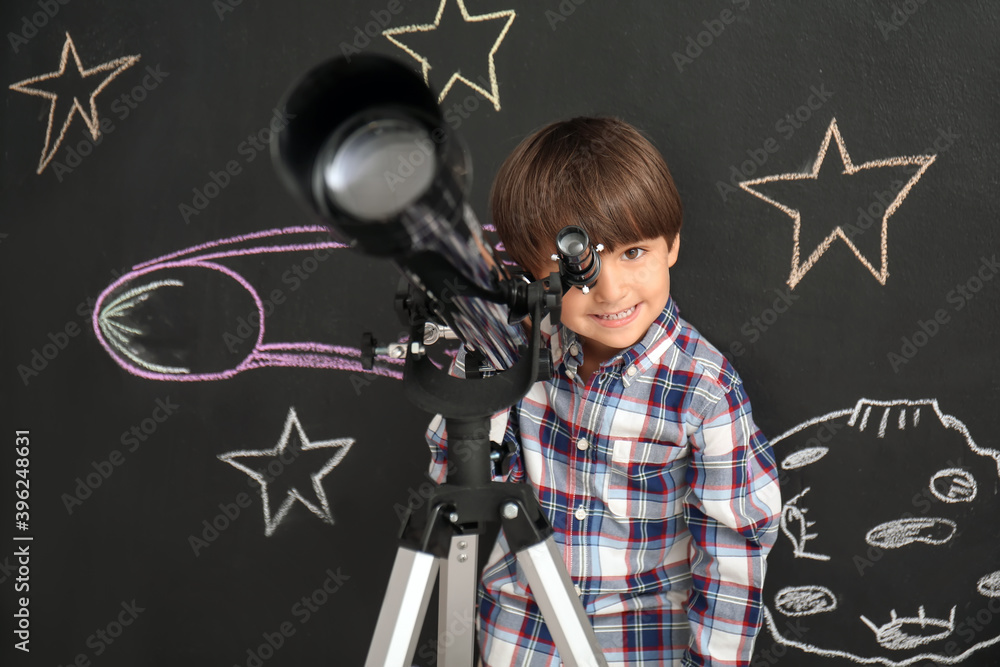 可爱的小男孩在望远镜里观察绘制空间的黑墙附近