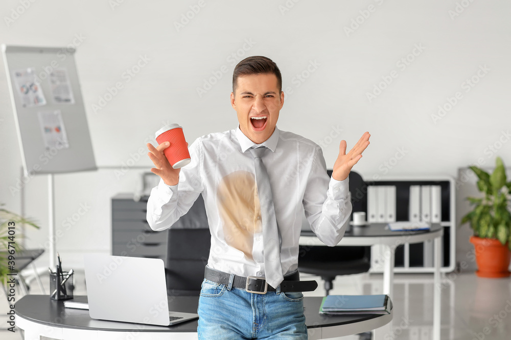 Screaming young businessman with coffee stains on his shirt in office