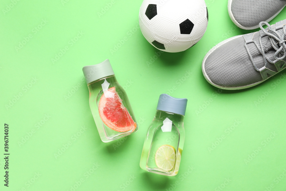 Bottles of infused water, sports shoes and soccer ball on color background