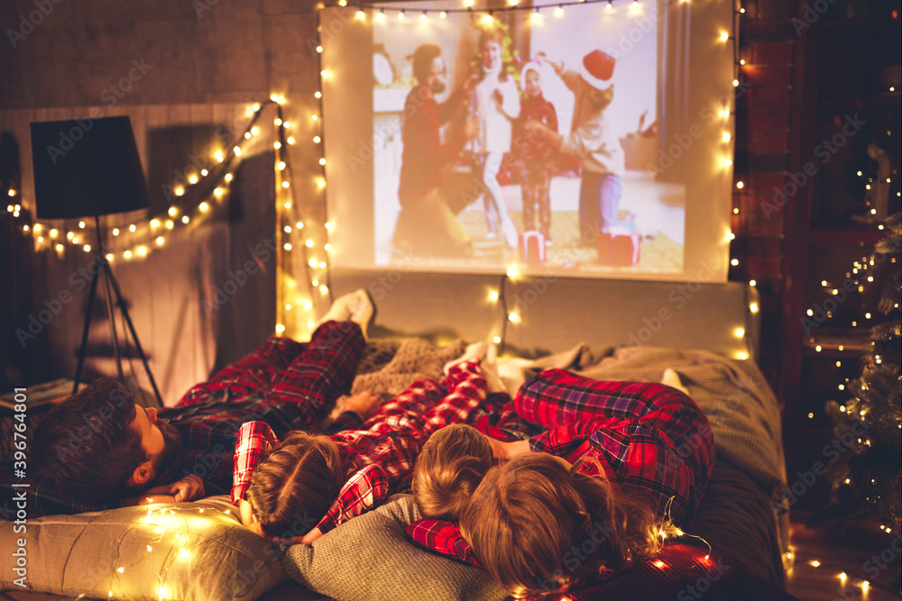 family mother father and children watching projector, TV, movies with popcorn in   christmas evening