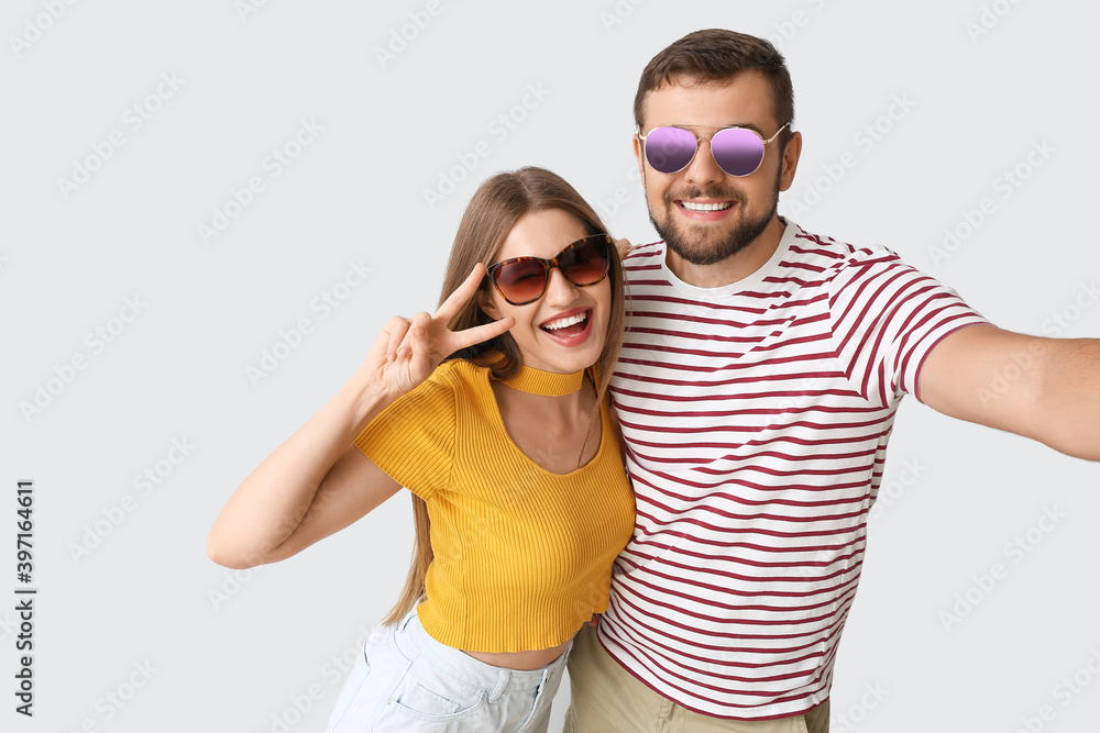 戴着时尚太阳镜的年轻情侣在浅色背景下自拍