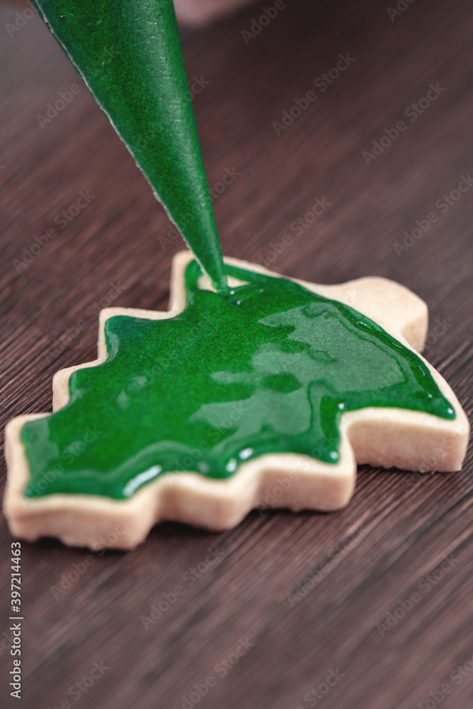 用糖霜在木桌背景上绘制圣诞树糖饼干的特写。