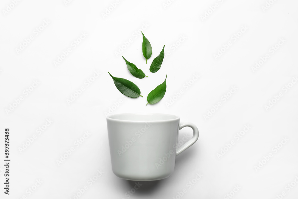 Cup and green tea leaves on white background