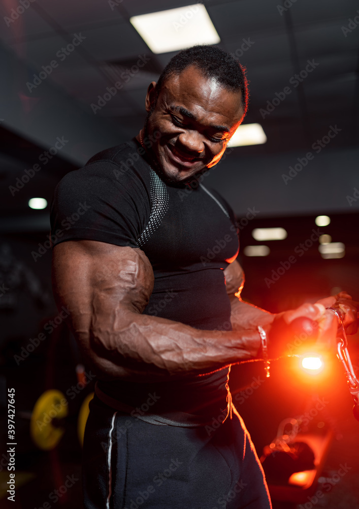 男子在健身房锻炼。现代健身房背景下穿着黑色衬衫的年轻男子的照片。力量