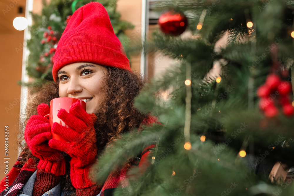 美丽的年轻女子在户外的圣诞树旁喝热茶
