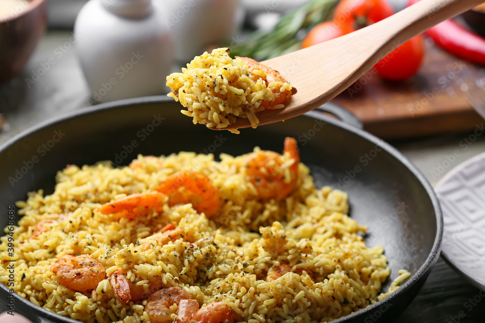 Frying pan with tasty pilaf and wooden spoon