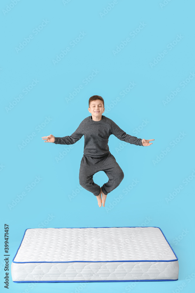 Meditating little boy jumping on mattress against color background