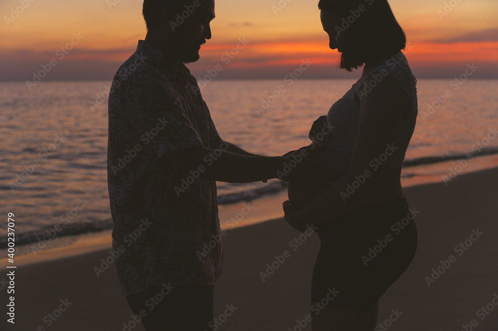年轻的家人和怀孕的妻子在日落时在海滩上度假。