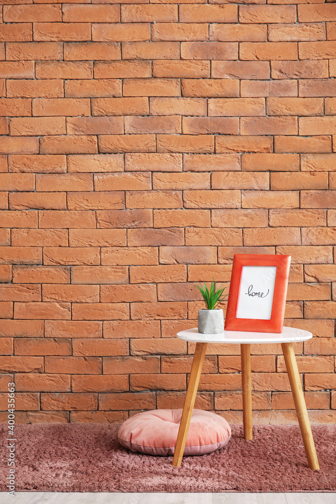 Stylish table with houseplant and photo frame near brick wall in room