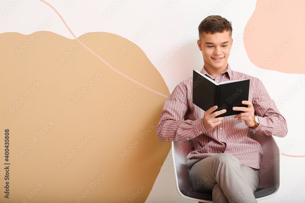 Teenage boy with book sitting near color wall