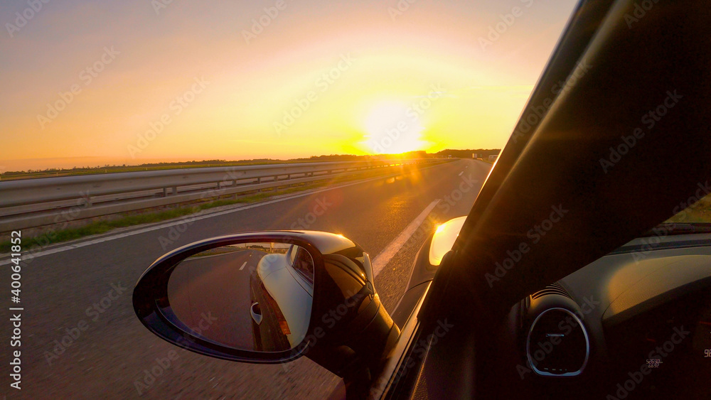 特写夏日傍晚，阳光照射在一辆行驶在空旷高速公路上的跑车上