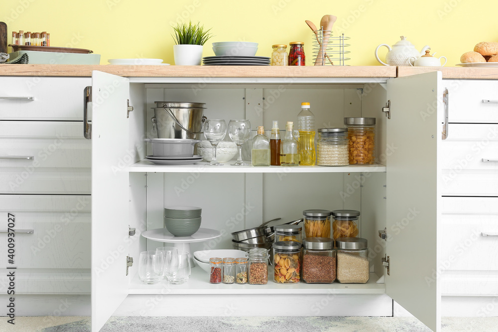 Shelves with utensils and glass jars with products in cupboard
