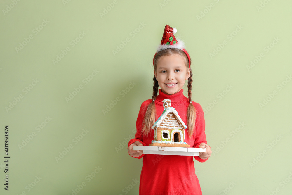 Happy little girl with gingerbread house on color background. Christmas celebration