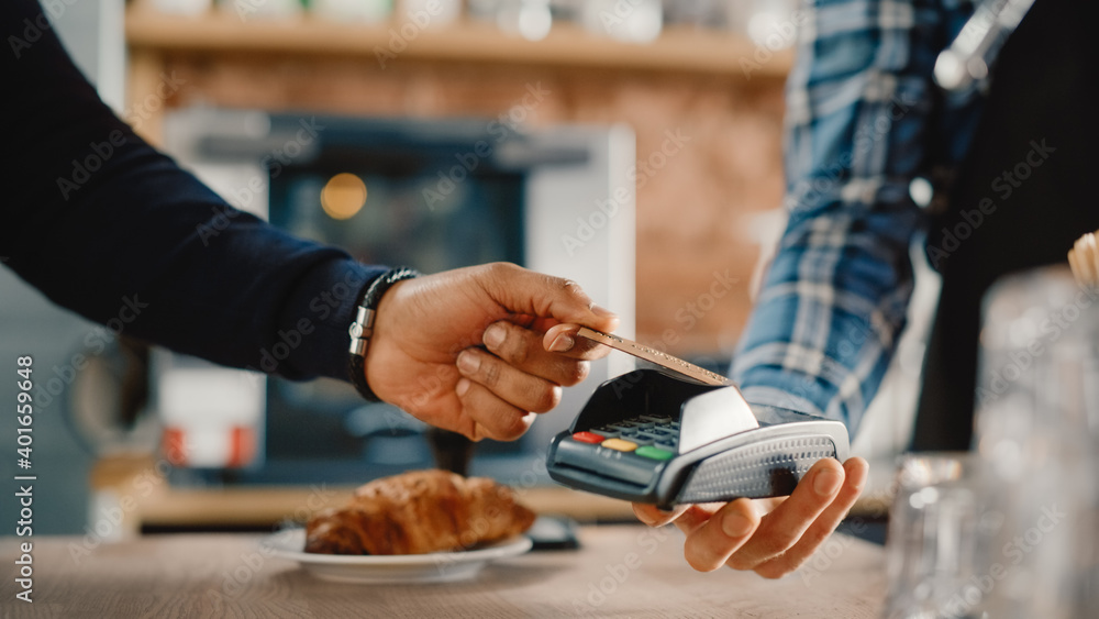 一只男性手拿着一张使用NFC支付技术的信用卡进行支付的特写