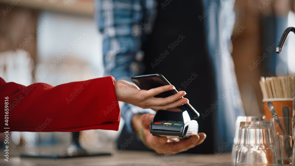 一只女性手拿着智能手机的特写镜头，该智能手机使用NFC支付技术进行支付