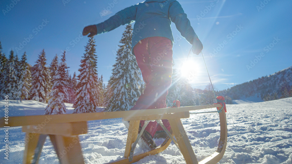 低角度：当一名妇女带着雪橇沿着雪地草地奔跑时，雪花在空中飞舞。