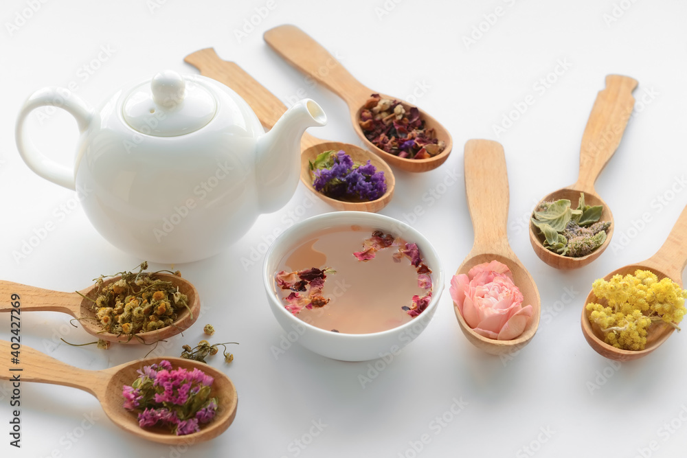 Dry flowers in spoons, teapot and cup with floral tea on light background