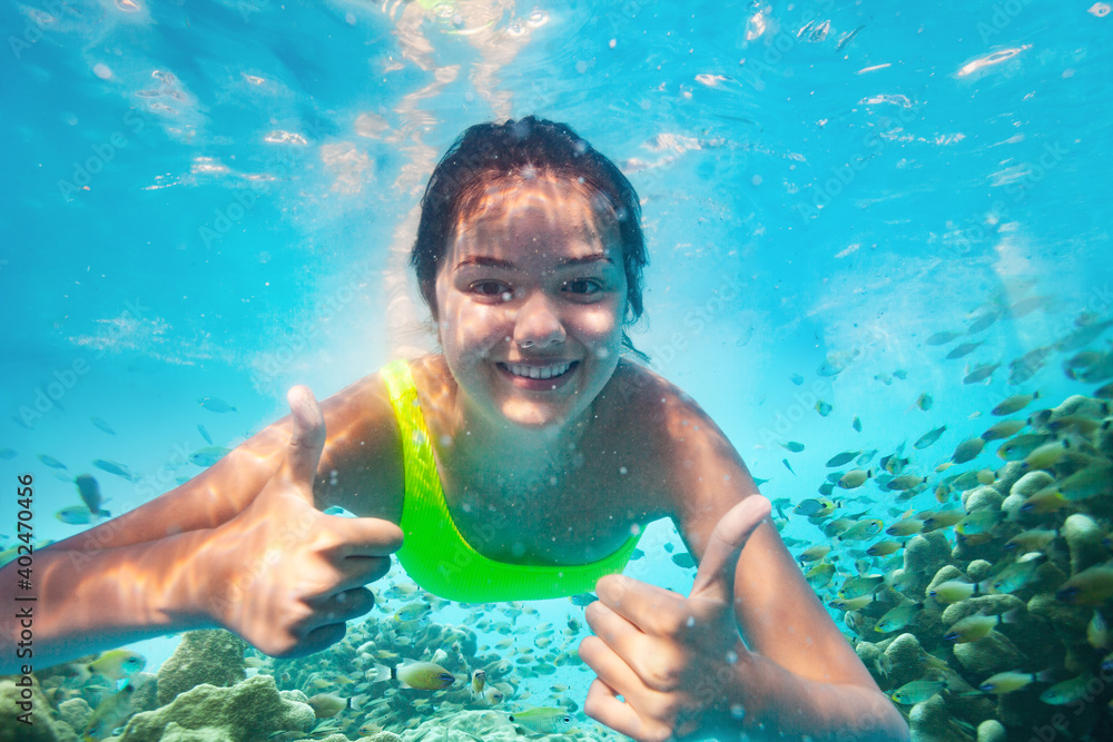 Happy smiling teen girl with v victory hands expression and big smile swim underwater between corals