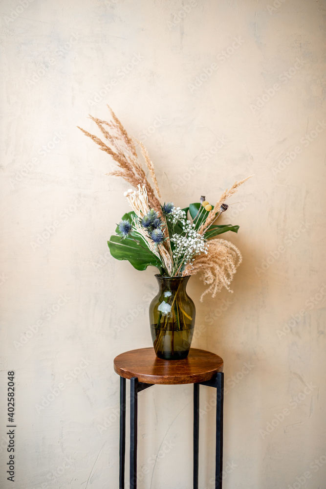 米色墙壁背景上的玻璃花瓶中的花朵和香草的成分。蒙斯特拉的气味，Cr