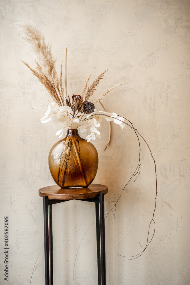 米色墙壁背景上的玻璃花瓶中的干花和香草的成分。潘帕斯的气味