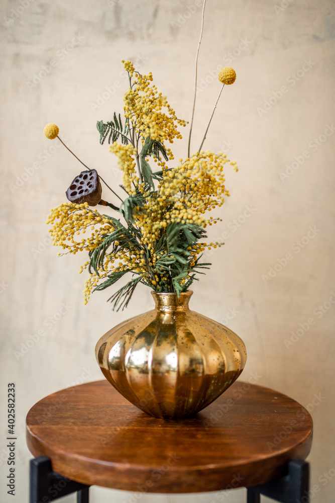 米黄色背景的金花瓶中的鲜花和草本植物组成。相思树的花束，