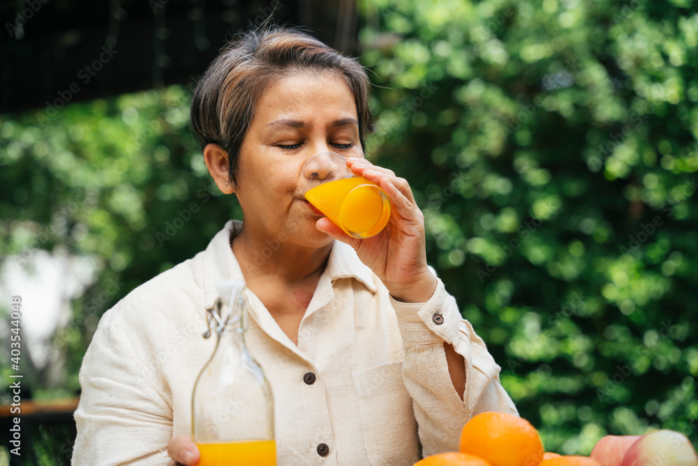 公园里，一位老年妇女在户外用玻璃杯喝橙汁。
