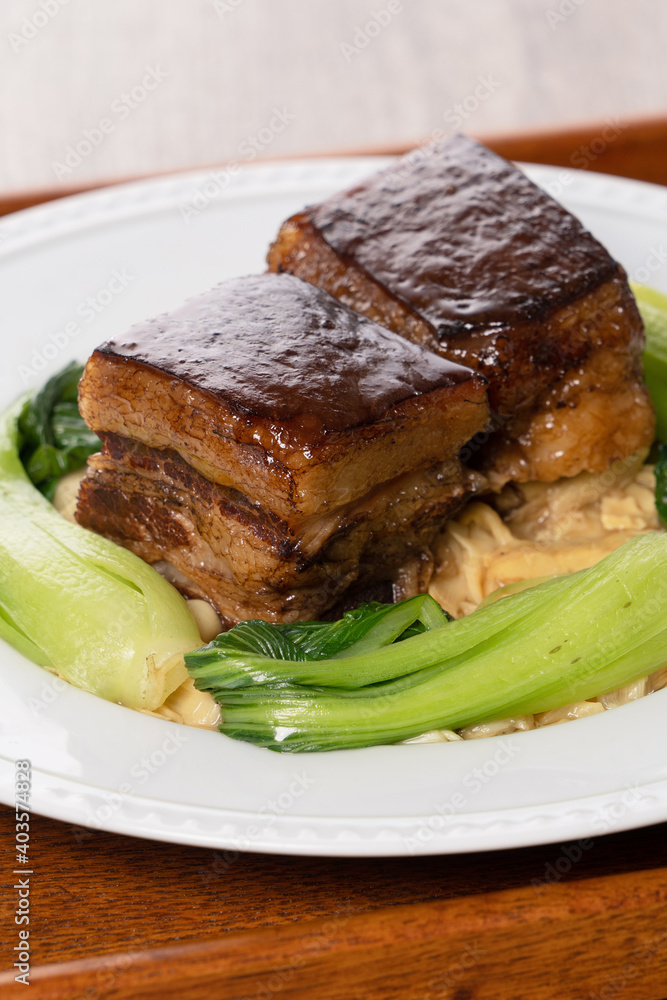 东坡肉装在白色盘子里，木质背景是蔬菜。