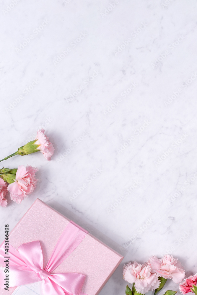 大理石白色桌子背景上美丽的康乃馨和礼物的俯视图。