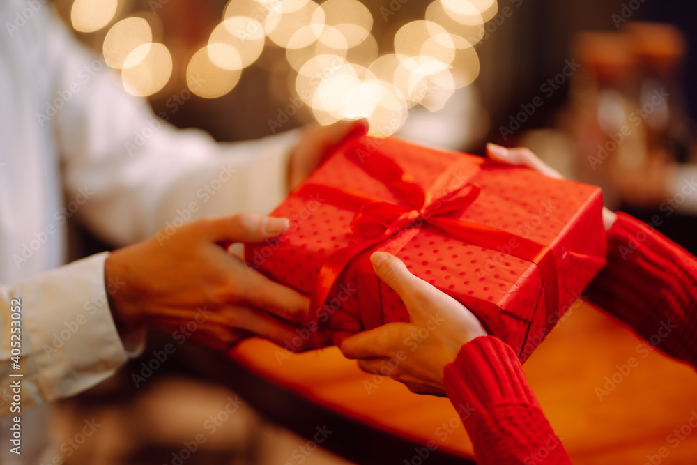 交换礼物。男人给他的女人一个带红丝带的礼物盒。年轻的恩爱夫妻