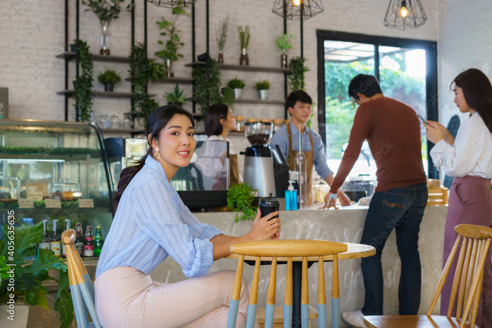亚洲女人坐在咖啡馆里，一边喝咖啡一边感到快乐，另一个人在排队