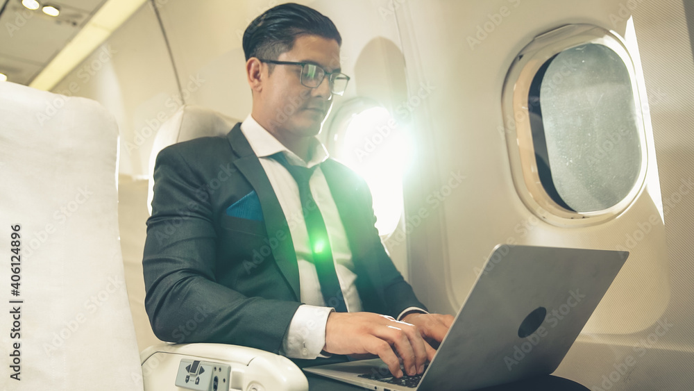 年轻的商人在飞机上使用笔记本电脑。商务旅行的概念。