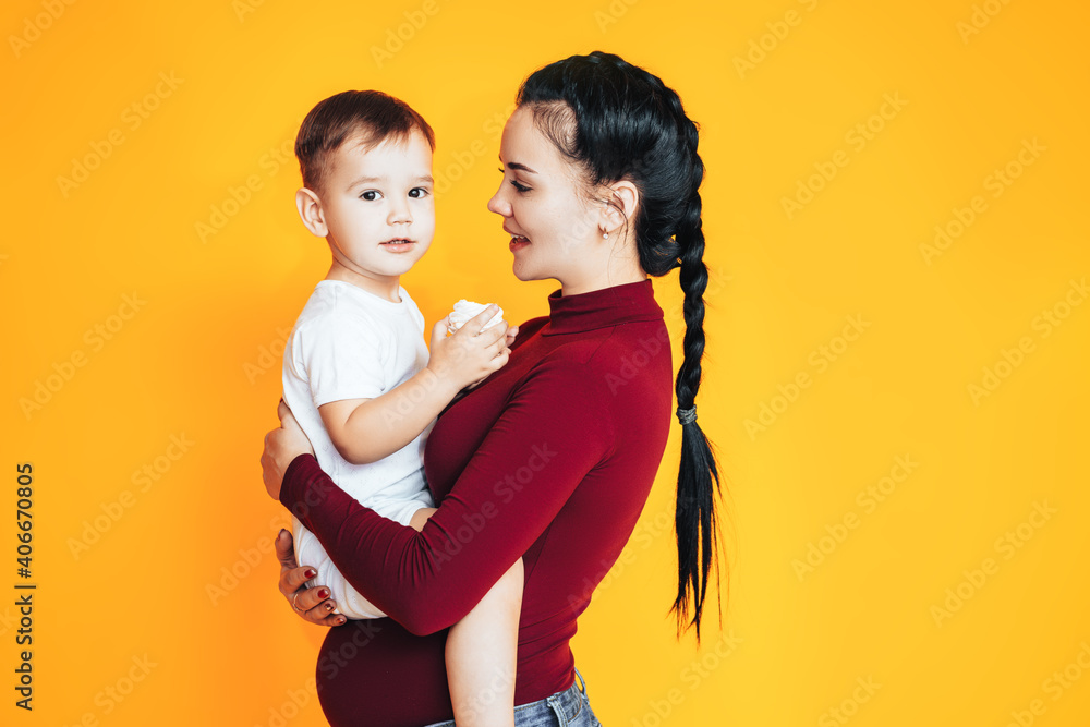 Pregnant young woman holding a small baby in front of a yellow background. Caring for the health of 
