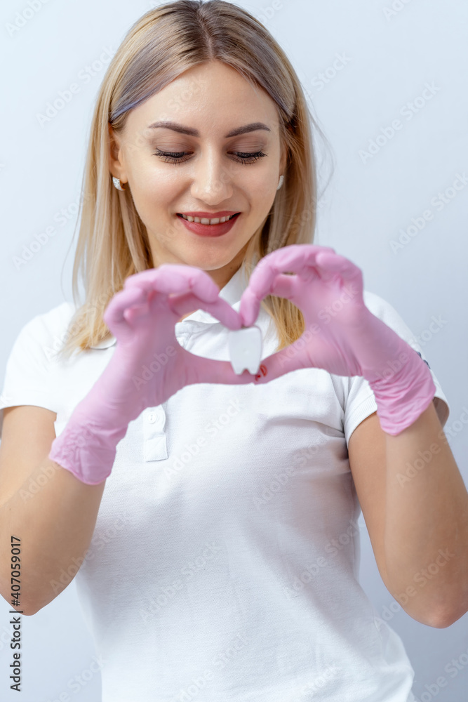 一位美丽的女牙医看着手中假牙的肖像。心形。口腔医学