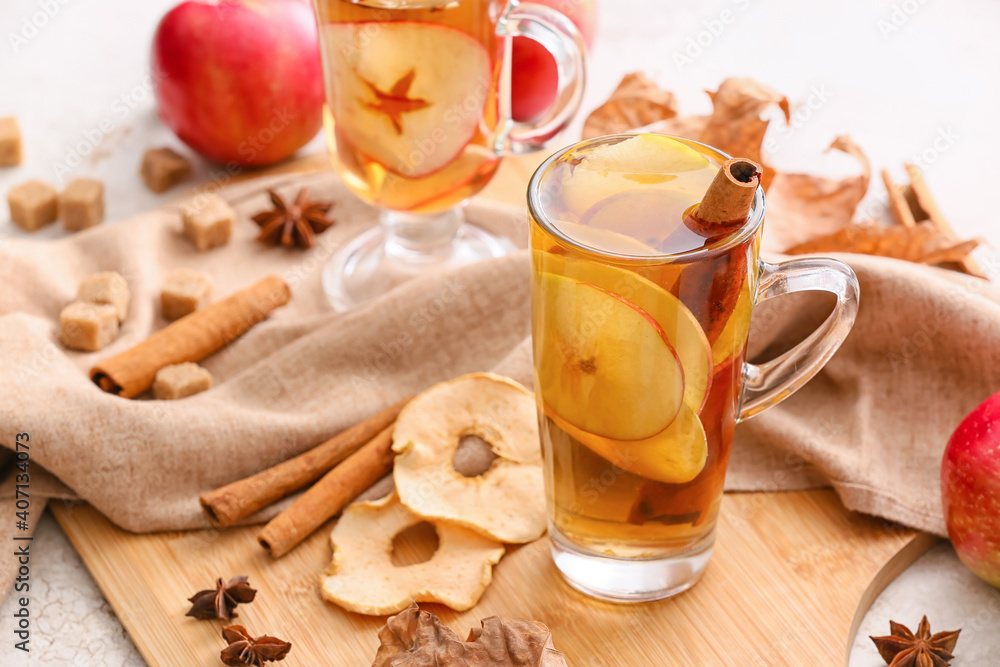 Tasty drink with spices and apple slices in cup on light table