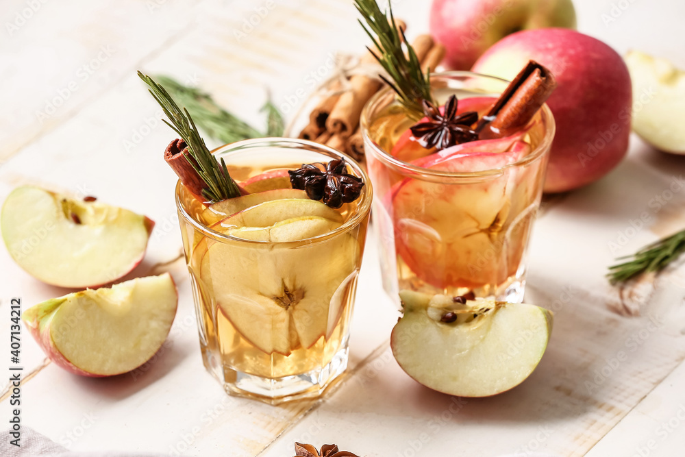 在浅色木质背景下，用玻璃杯装着香料和苹果片的美味饮料
