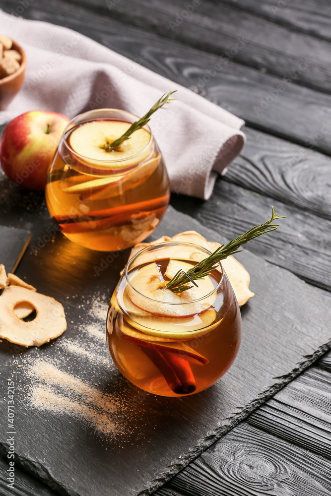 在深色木质背景下，用玻璃杯装着香料和苹果片的美味饮料