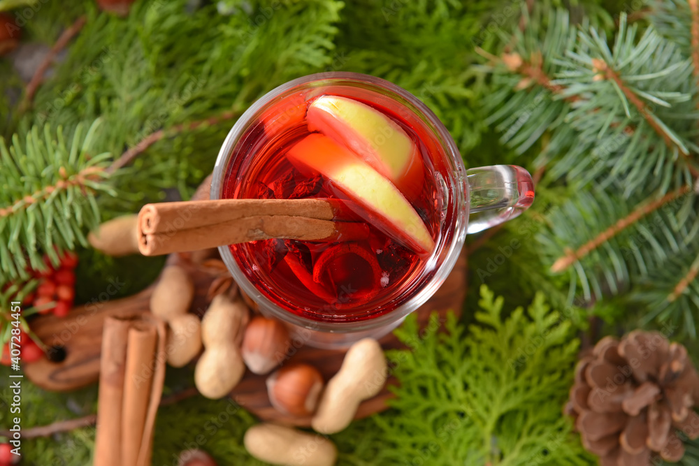 Tasty mulled wine with cinnamon in glass on Christmas tree branches