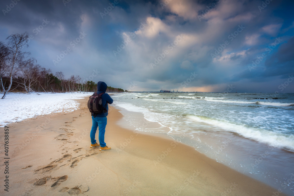 一个男人在下雪的冬天在海滩上看波罗的海。波兰格但斯克