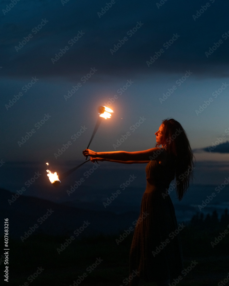 优雅优雅的红发女消防表演演员用点燃的两个金属风扇跳火舞