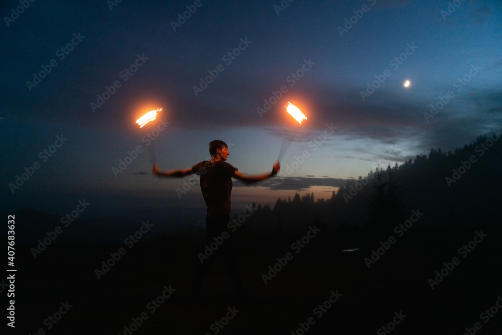 优雅的男性消防表演表演者在夜晚与点燃火焰的两个金属风扇跳火舞